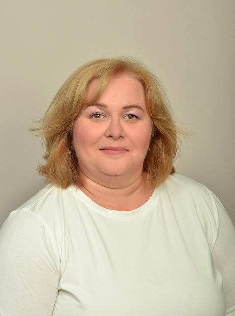 Branka Haupka-Miljkovic, eine weiße Frau mit schulterlangen blonden Haaren, trägt ein weißes T-Shirt und lächelt in die Kamera.