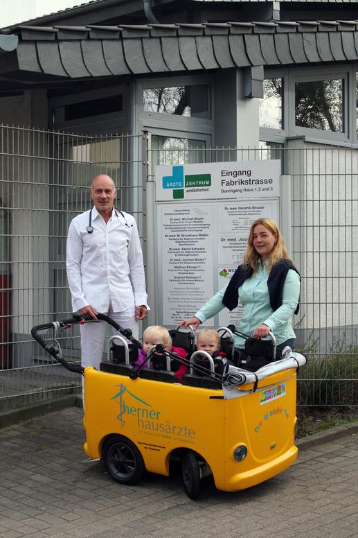 Dr. Bruckhaus-Walter mit dem Kindermobil; einem gelben Wagen, in dem zwei Kinder sitzen.