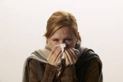 Frau putzt sich die Nase mit einem Taschentuch.