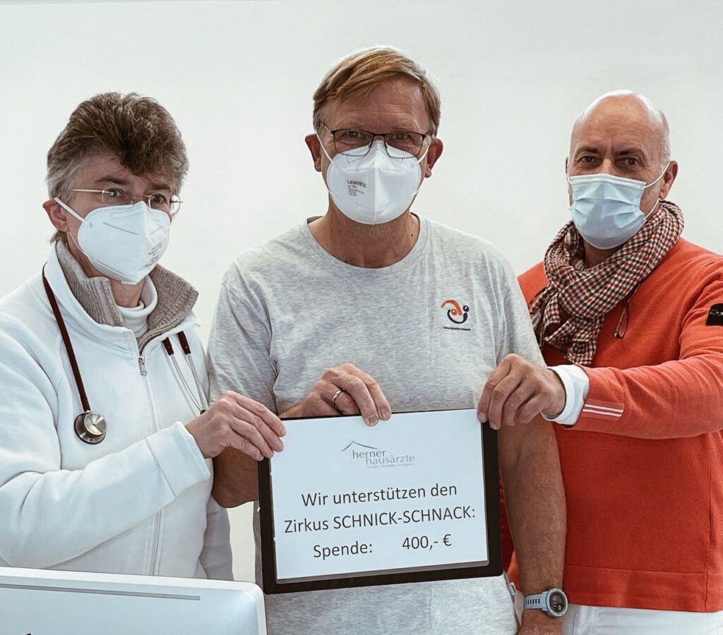 Zirkusdirektor Rainer Deutsch hält gemeinsam mit Dr. Bruckhaus-Walter und Dr. Schwarz ein Schild hoch mit der Aufschrift "Wir unterstützen den Zirkus Schnick-Schnack: Spende: 400 Euro.".