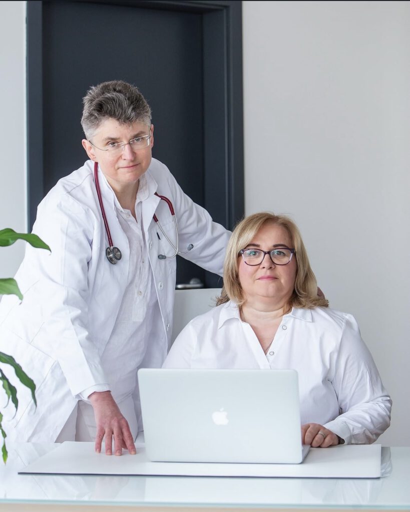Screenshot Frau Dr Schwarz und Frau Haupka sind nebeneinander vor einem Laptop positioniert. Lächeln freundlich.